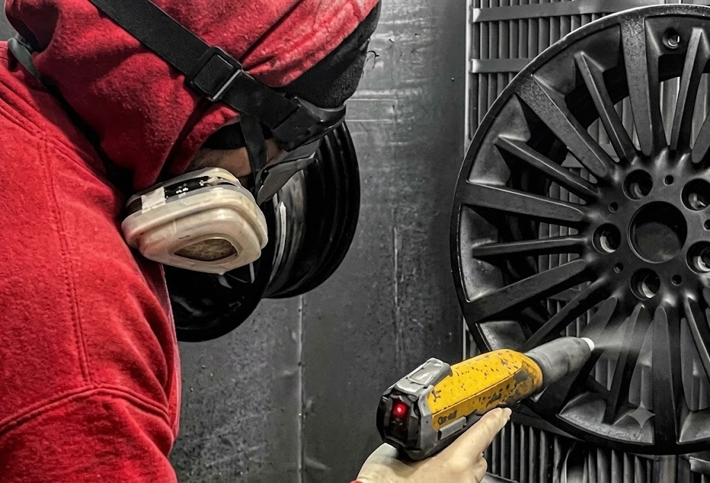 Technician powder coating an alloy wheel in the spray booth